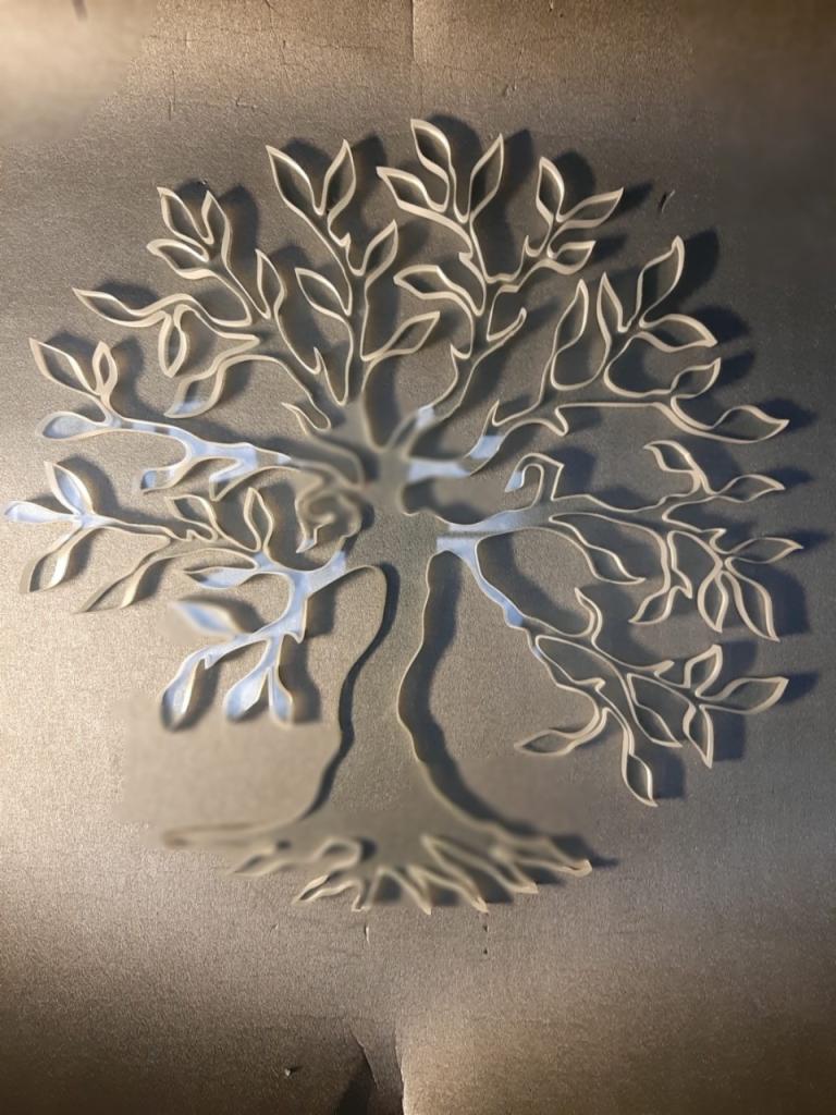 Delikatna, przestrzenna dekoracja ścienna w kształcie drzewa z liśćmi, wykonana z jasnego materiału na ciemnym, teksturowanym tle. Kontury drzewa są wyraźnie zarysowane, tworząc efekt...