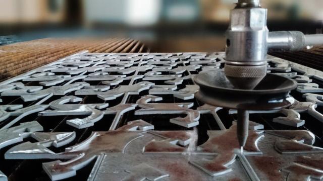 Precyzyjne cięcie plazmowe metalowej płyty z powtarzalnym wzorem dekoracyjnym, detale wykonane z dbałością o szczegóły, w tle widoczna konstrukcja hali.