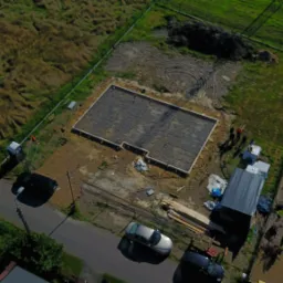 Zdjęcie z drona przedstawia zbrojenie fundamentów domu jednorodzinnego na działce, widoczne samochody pracowników i tymczasowe zaplecze budowy.