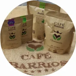 Trzy papierowe torby z kawą Cafe Barrios Guatemala o różnej gramaturze (250g, 500g, 1000g) ustawione na worku jutowym z nadrukowanym logo firmy.