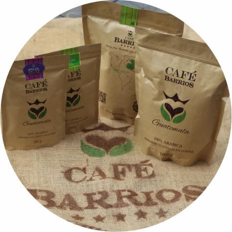 Trzy papierowe torby z kawą Cafe Barrios Guatemala o różnej gramaturze (250g, 500g, 1000g) ustawione na worku jutowym z nadrukowanym logo firmy.