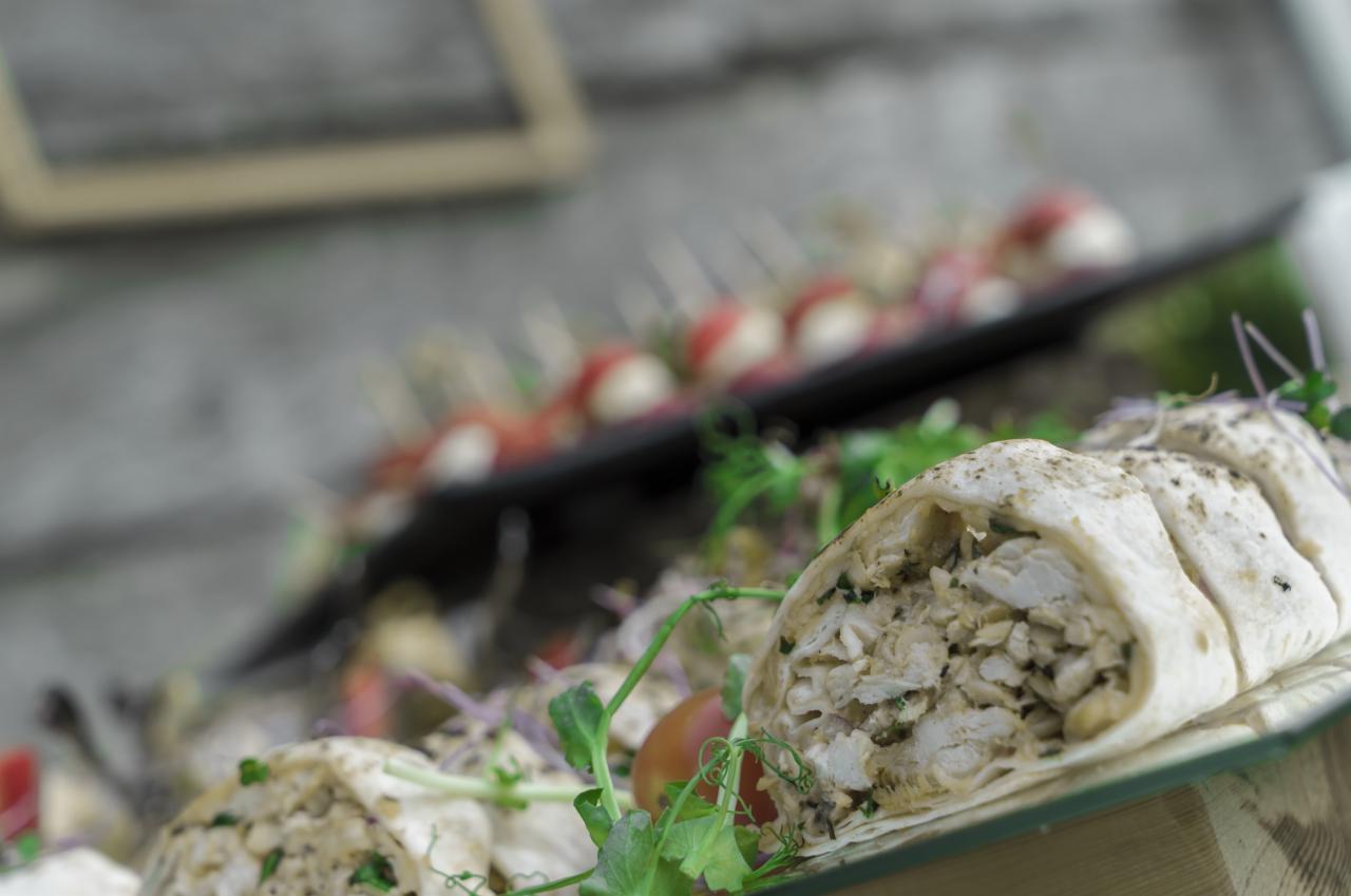 Tortilla z kurczakiem i warzywami na szklanej tacy, serwowana jako przekąska cateringowa w Łodzi, z widocznymi w tle koreczkami z pomidorkami i mozzarellą.