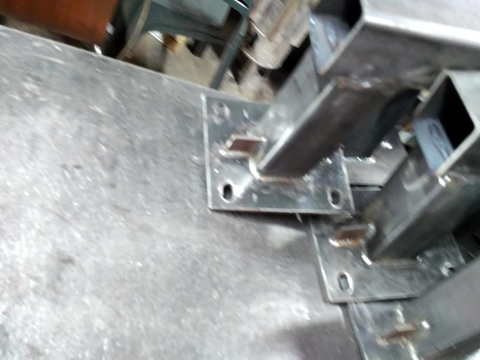 Spawane elementy konstrukcyjne z metalowych profili kwadratowych i blach, widoczne spawy i otwory montażowe, surowy metal.