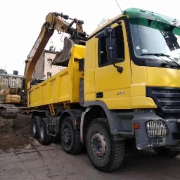 Żółta wywrotka Mercedes i koparka CAT w tle, podczas załadunku ziemi na placu budowy w mieście.