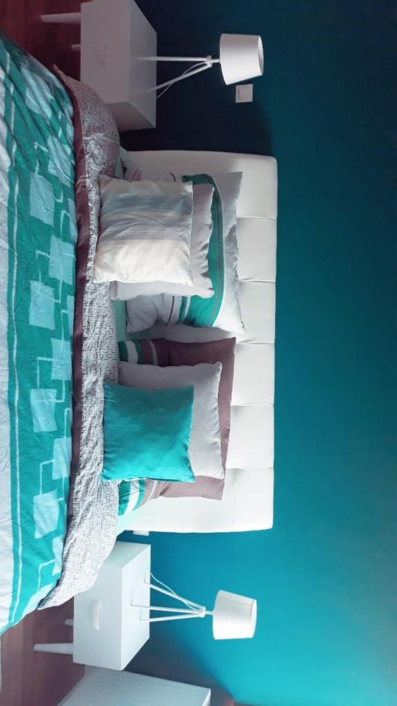 Sypialnia w odcieniach turkusu i bieli z łóżkiem z pikowanym zagłówkiem, nocnymi szafkami i lampkami nocnymi, widok z góry.