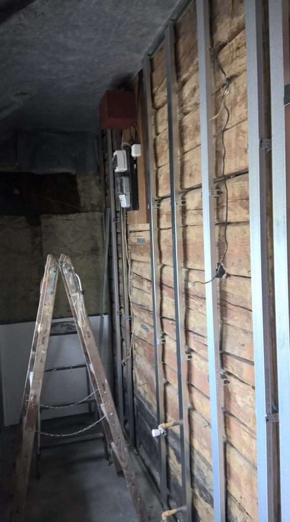 Ściana z drewnianą boazerią w trakcie montażu stelażu metalowego, widoczne instalacje elektryczne i drabina