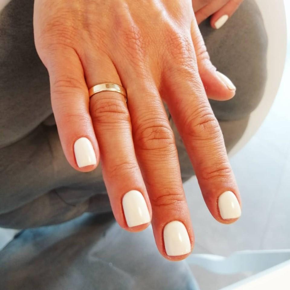 Dłoń kobiety z białym manicure hybrydowym i złotym pierścionkiem na palcu serdecznym, widok z bliska.