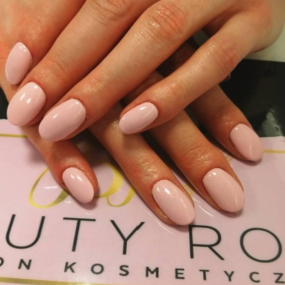 Dłonie po manicure hybrydowym w odcieniu pudrowego różu, ułożone na wizytówce salonu kosmetycznego.