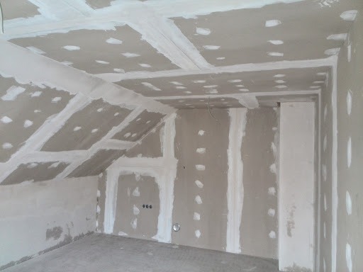 Poddasze z zamontowanymi płytami gipsowo-kartonowymi, widoczne łączenia szpachlowane na suficie skośnym i ścianach, przygotowane do dalszych prac wykończeniowych.