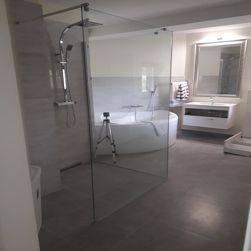 Nowoczesna łazienka z kabiną prysznicową typu walk-in, owalną wanną i wiszącą szafką z umywalką, sfotografowana ze statywem w tle.