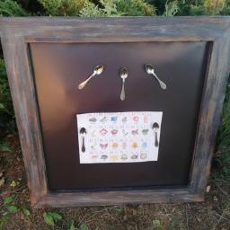 DariaSworowska - Tablica edukacyjna w drewnianej ramie, z literami alfabetu i obrazkami, przyczepiona do czarnej magnetycznej powierzchni za pomocą czterech srebrnych łyżeczek.