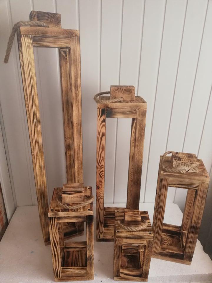 Ręcznie robione drewniane lampiony w różnych rozmiarach, z efektem przypalenia i sznurkowymi uchwytami, ustawione na białym tle.