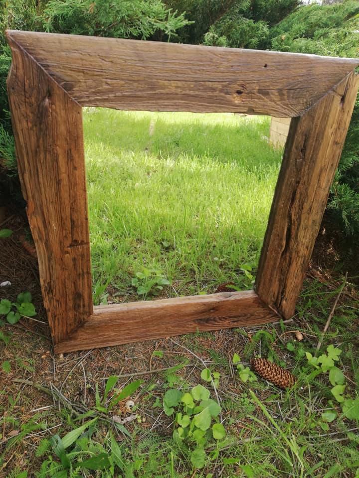 Rustykalna rama z surowego drewna, ustawiona na trawie z widoczną szyszką i zielenią w tle.