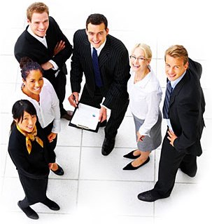 Grupa uśmiechniętych, różnorodnych etnicznie pracowników biurowych w formalnych strojach, patrzących w górę w obiektyw. Jeden mężczyzna trzyma notatnik i długopis. Biała podłoga w tle.