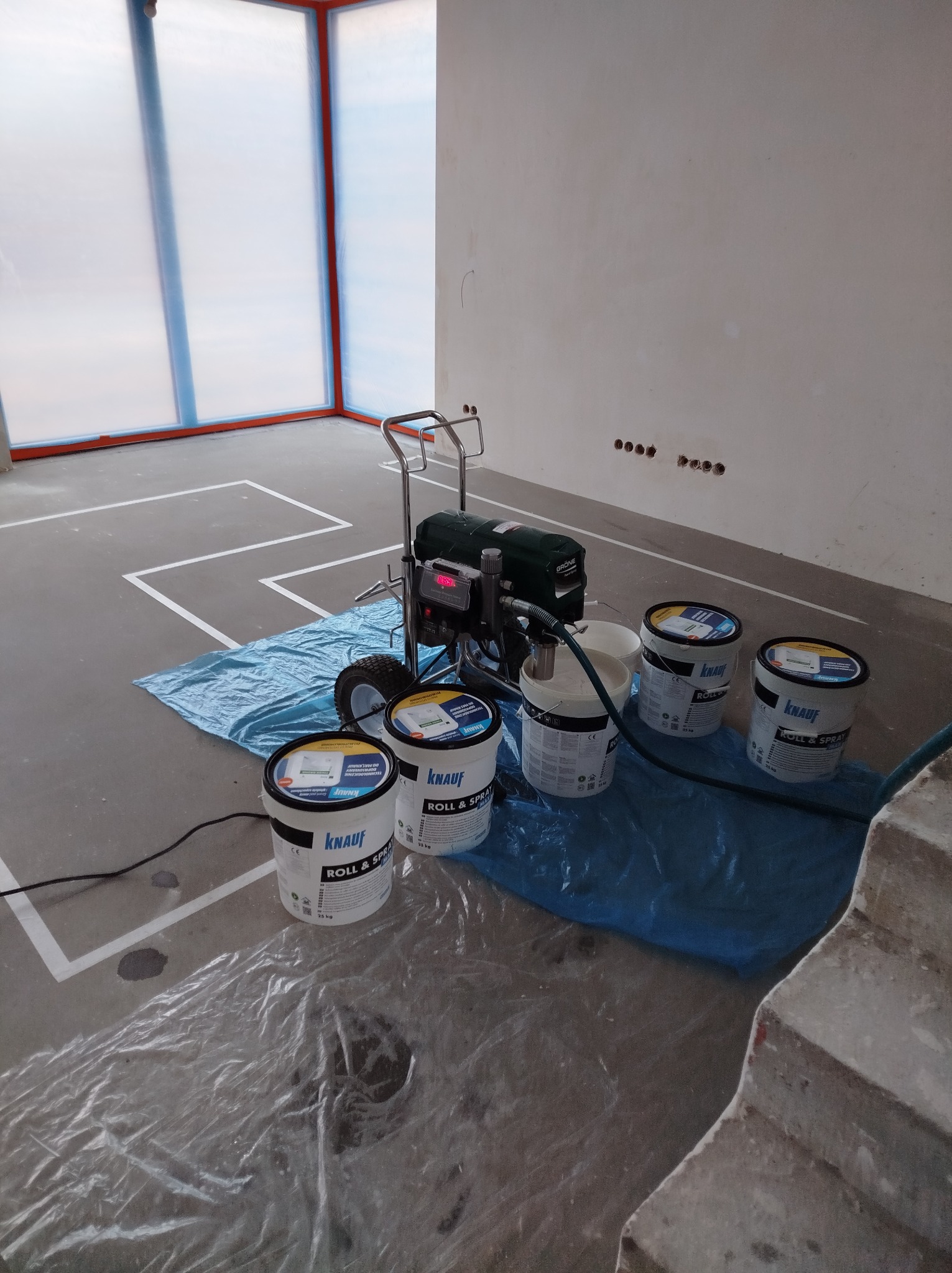 Przygotowania do natryskowego nakładania gładzi: agregat malarski, kilka wiader z gładzią Knauf Roll & Spray, folia ochronna na podłodze i oknach, wyznaczone linie.