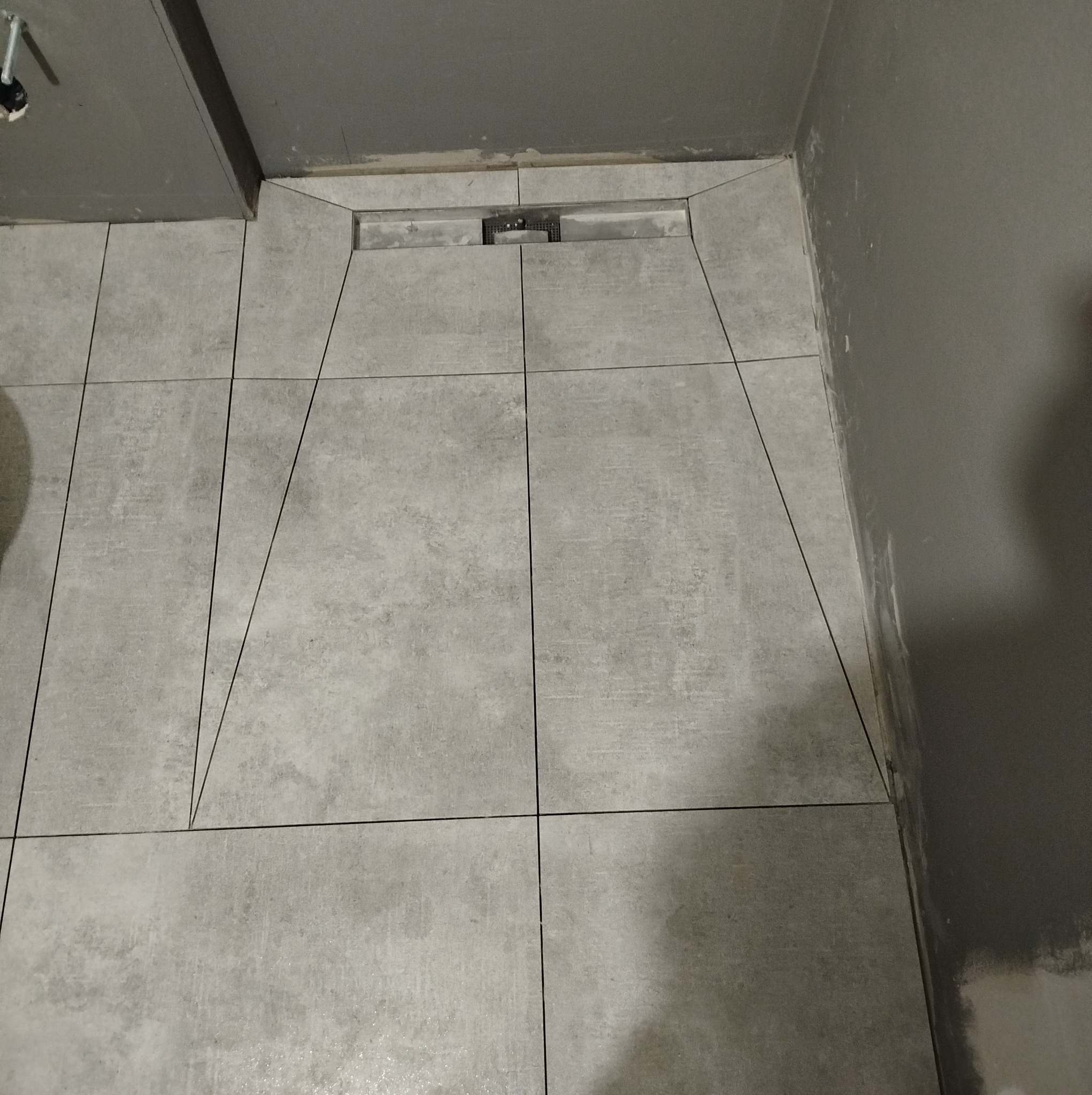 Ułożone szare płytki podłogowe w łazience z odpływem liniowym, widoczne niedociągnięcia przy ścianie