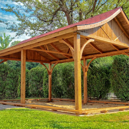 Happy Garden - Drewniana konstrukcja z czerwonym dachem w ogrodzie, widoczne elementy wykończeniowe i logo Happy Garden w prawym dolnym rogu.