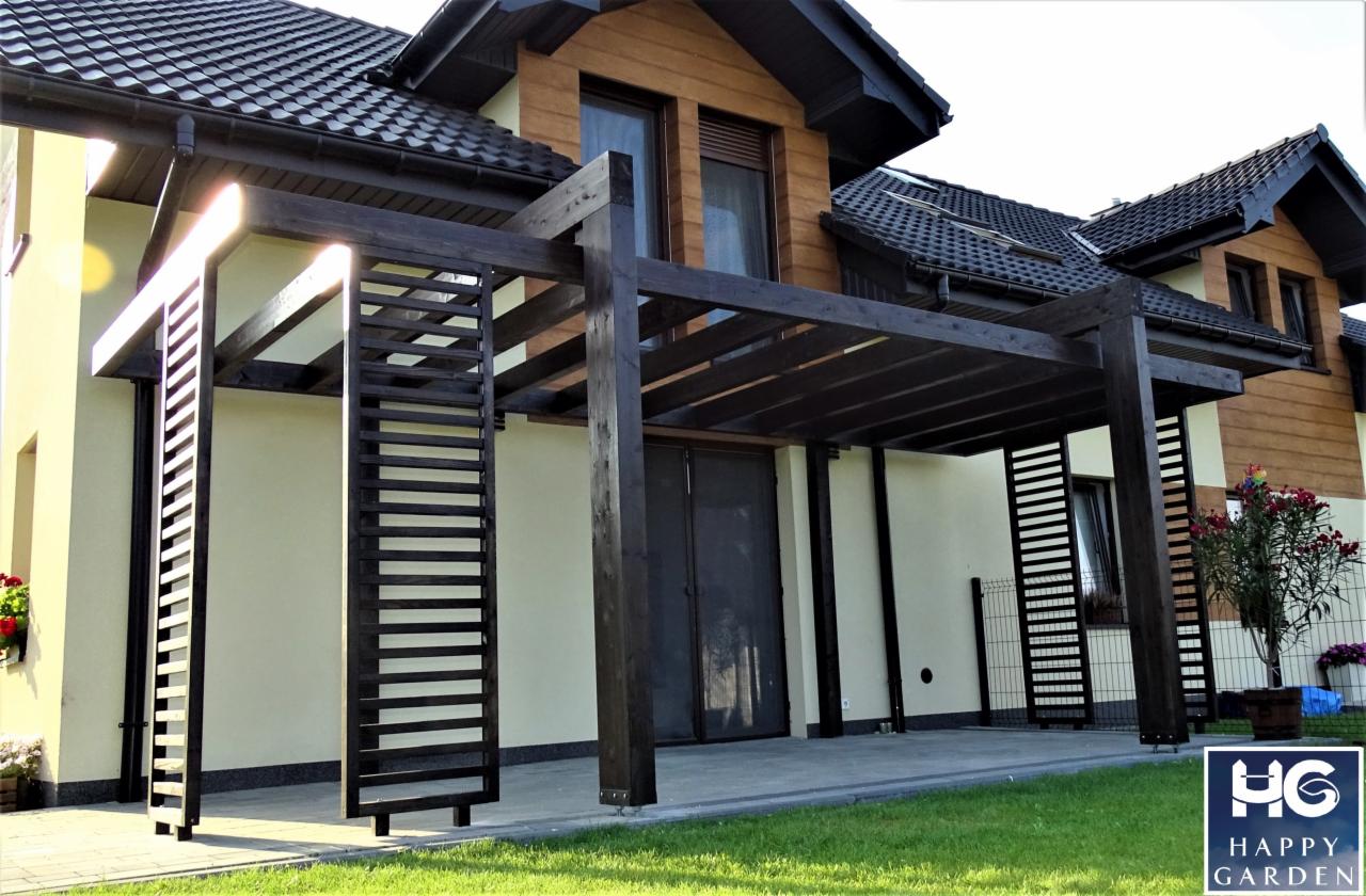 Nowoczesna pergola drewniana w kolorze ciemnego brązu, przylegająca do domu z jasną elewacją i ciemnym dachem, z elementami dekoracyjnymi w postaci drewnianych paneli z poziomymi szczebelkami.