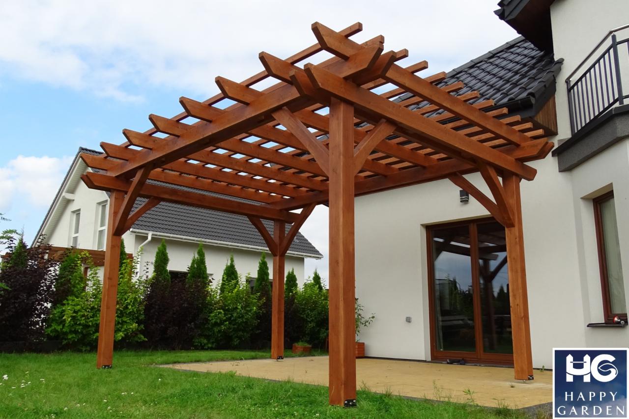 Drewniana konstrukcja z belek, tworząca zadaszenie nad tarasem, z widocznym ogrodem i fragmentem domu w tle.