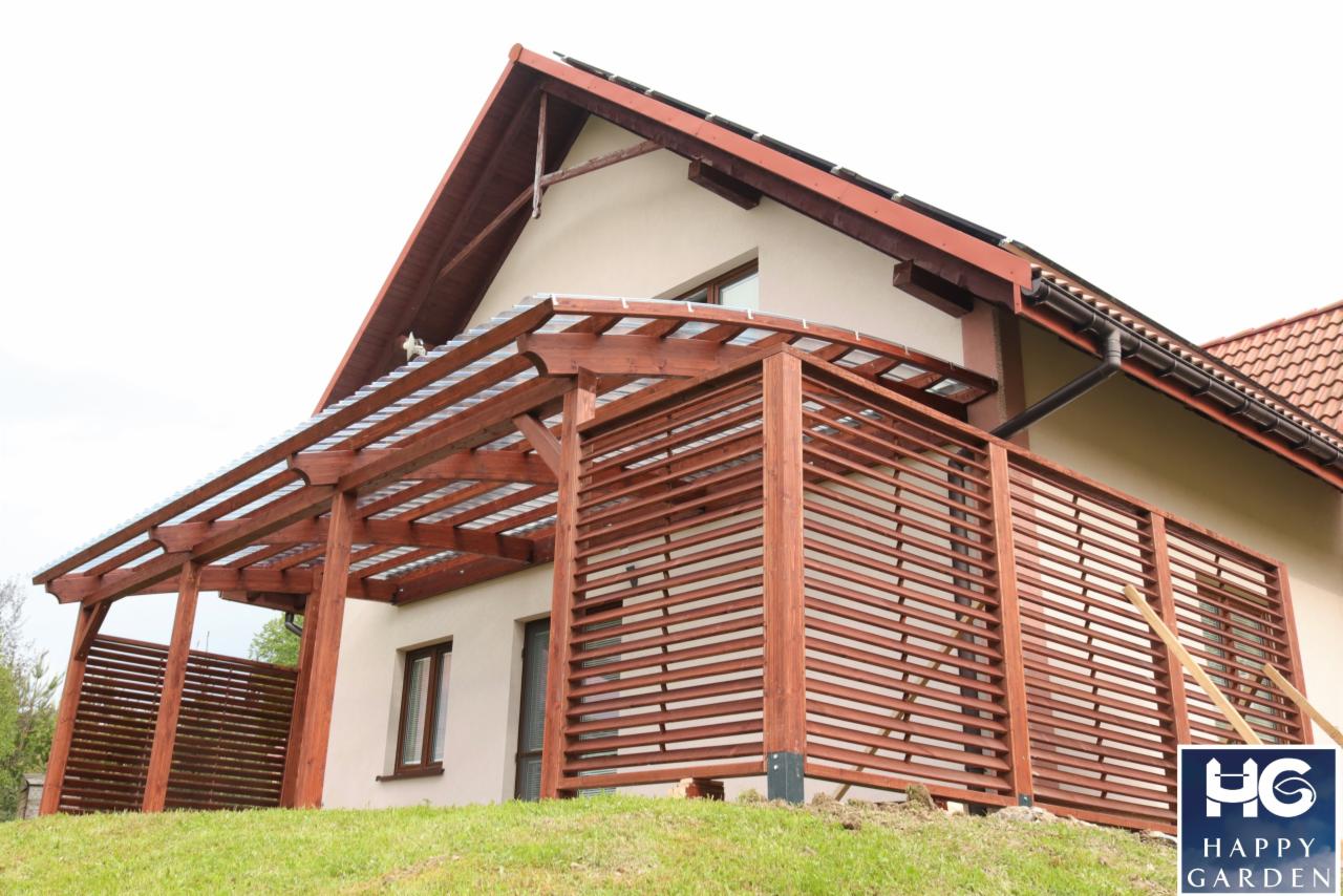 Drewniana pergola z ażurowymi ścianami przylegająca do domu z dwuspadowym dachem, pokryta przezroczystym zadaszeniem, widoczna z poziomu trawnika.