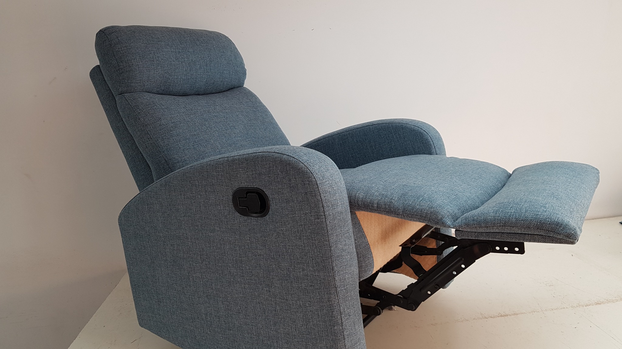 Rozłożony, tapicerowany fotel relaksacyjny w odcieniach niebieskiego z widocznym mechanizmem rozkładania, sfotografowany na jasnym tle.