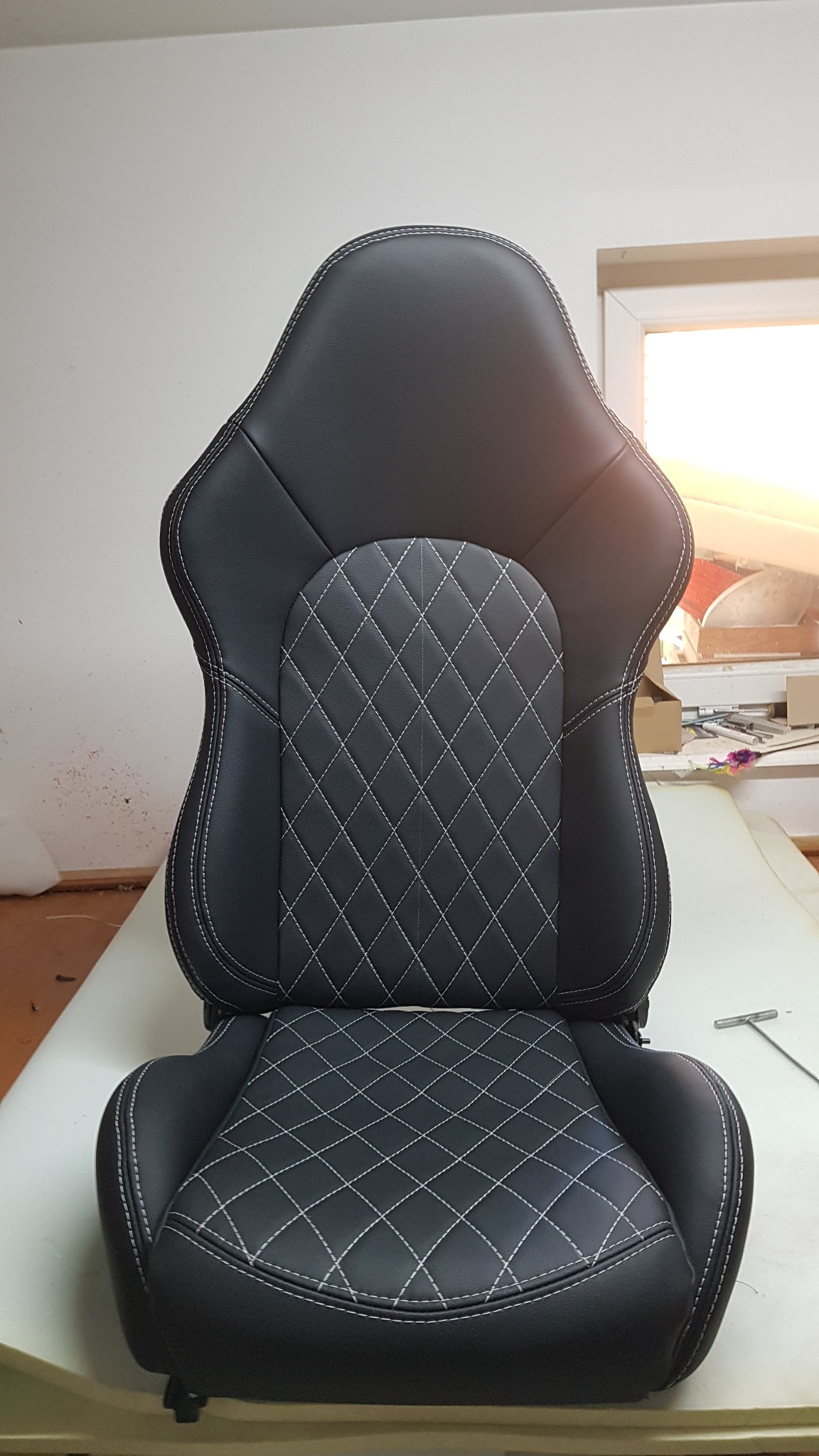 Czarne, skórzane siedzisko fotela z białymi przeszyciami w romby, widoczne na jasnym stole w warsztacie.