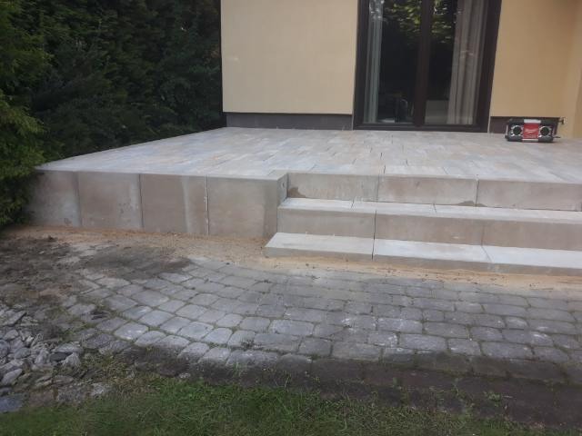 Wykończony taras betonowy z kilkoma schodami, widoczne kostki brukowe na ziemi oraz radio na tarasie