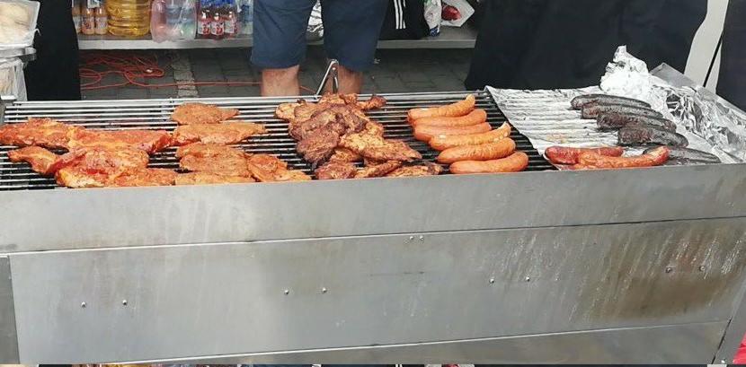 Przygotowywane na grillu mięsa i kiełbasy, część już upieczona, ułożone na folii aluminiowej, w tle widoczne butelki z napojami.