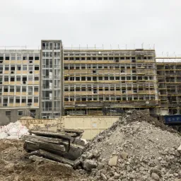 Widok na budynek w trakcie rozbiórki, z rusztowaniami, stertą gruzu, workami z odpadami i ciężarówką w tle.