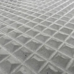 Szara, betonowa powierzchnia z regularnym wzorem piramid, sfotografowana pod kątem, ukazująca teksturę i detale konstrukcyjne.
