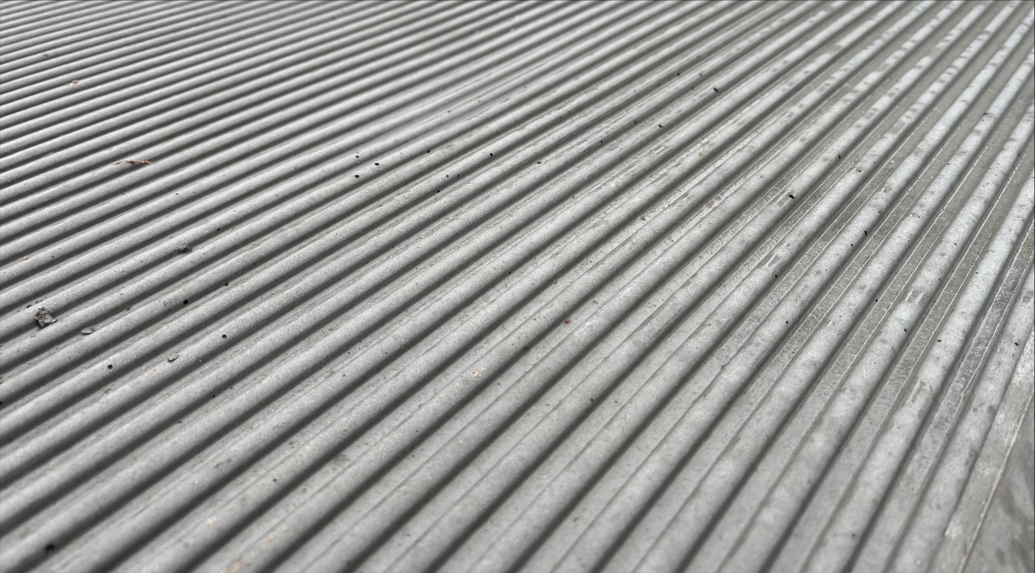 Szara, żebrowana powierzchnia betonowa z widocznymi drobnymi zabrudzeniami i resztkami organicznymi.