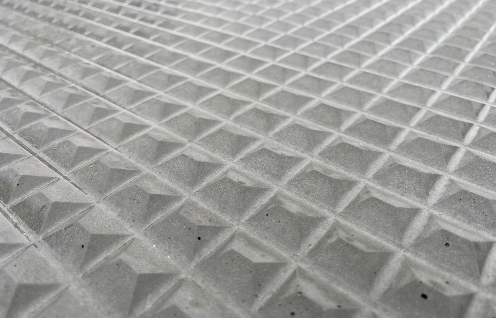 Szara, betonowa powierzchnia z regularnym wzorem piramid, sfotografowana pod kątem, ukazująca teksturę i detale konstrukcyjne.