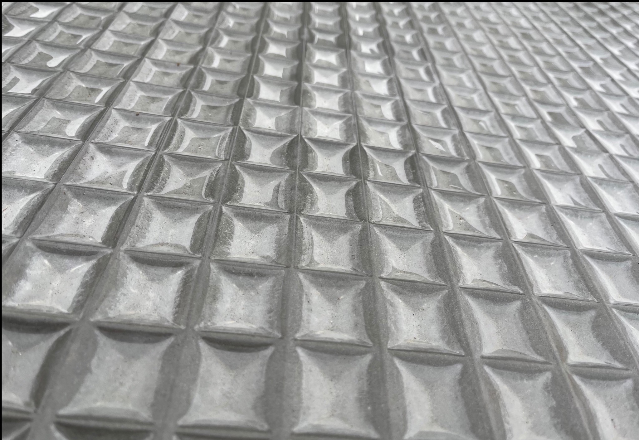 Szorstka, betonowa powierzchnia z regularnym wzorem kwadratowych wgłębień, sfotografowana pod kątem, ukazująca teksturę i perspektywę.