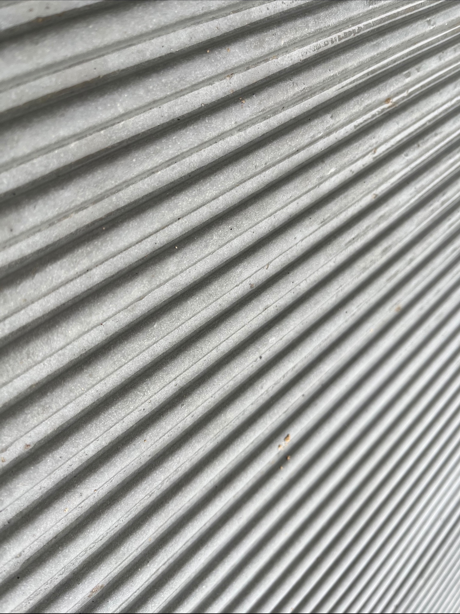 Szara, żebrowana powierzchnia pod kątem, prawdopodobnie element konstrukcyjny z betonu lub innego materiału budowlanego.