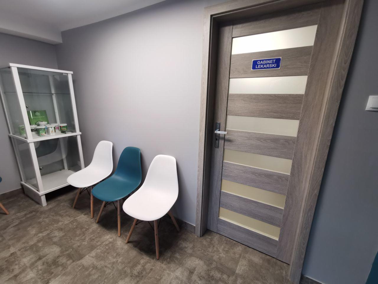 Poczekalnia gabinetu weterynaryjnego: trzy krzesła (dwa białe, jedno turkusowe) ustawione obok przeszklonej witryny z produktami, drzwi z napisem 'Gabinet Lekarski'.