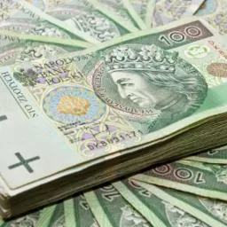 Stos banknotów 100 złotych na tle rozłożonych banknotów, widoczny numer seryjny DK8891171.