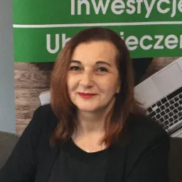 Portret kobiety z czerwonymi ustami na tle biurowym z napisem 'Inwestycje Ubezpieczenia' i laptopem