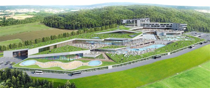 Wizualizacja kompleksu hotelowo-rekreacyjnego z zielonym dachem, basenami i zewnętrzną strefą relaksu, otoczonego lasami i polami, widziana z lotu ptaka.