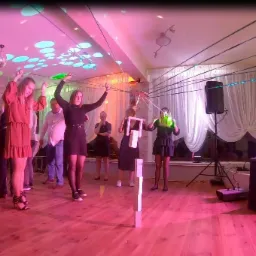 Goście weselni biorący udział w zabawie z linami i przeszkodami, oświetlenie sceniczne w odcieniach różu i zieleni, parkiet taneczny.