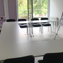 Ivanov Sp. z O. o - Jasne biuro z widokiem na las, białe stoły konferencyjne i czarne krzesła, flipchart przy ścianie, światło wpadające przez otwarte drzwi balkonowe.