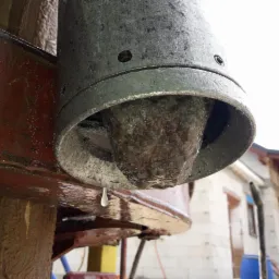 Wiertnica do studni abisyńskiej w trakcie pracy, widoczny wypływający urobek i kropla wody, w tle budynek w trakcie budowy.