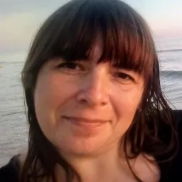 Portret uśmiechniętej kobiety z mokrymi włosami na tle morza o świcie.