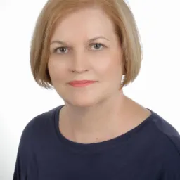 Portret kobiety o jasnych włosach, ubrana w granatową bluzkę, na jasnym tle. Profesjonalny wizerunek, budzący zaufanie.