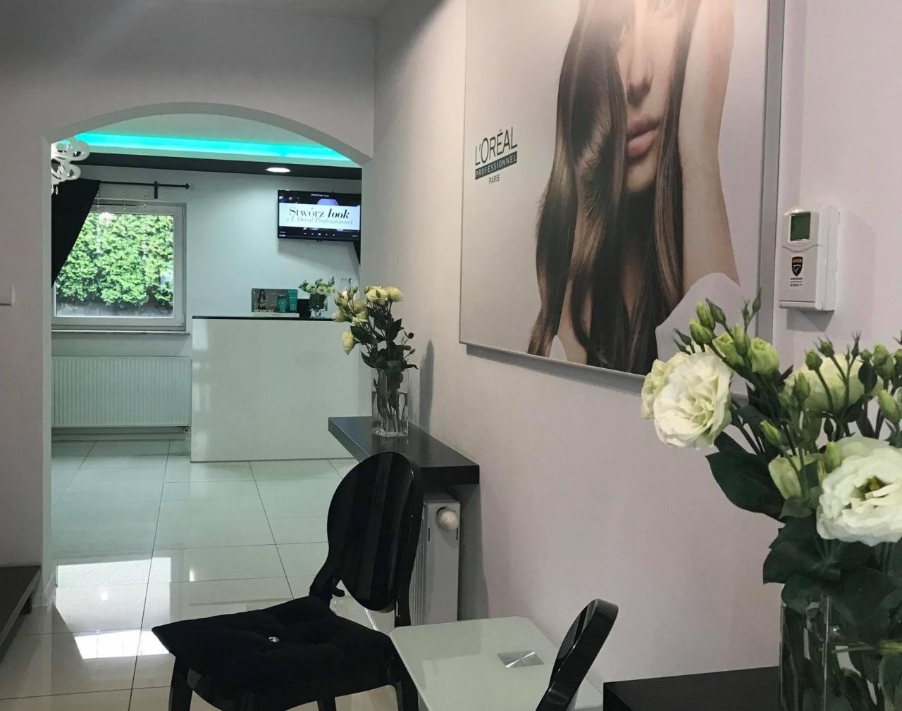 Wnętrze salonu z recepcją, kwiatami w wazonie i plakatem L'Oreal na ścianie, widok z poczekalni.