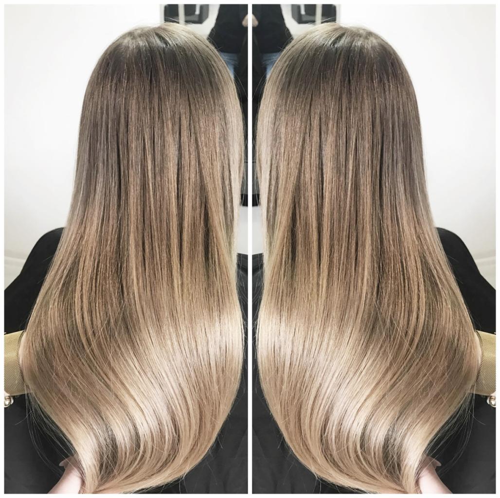 Długie, proste włosy z ombre, przechodzące od ciemnego blondu u nasady do jasnego blondu na końcach, widoczne z tyłu, z delikatnym połyskiem.