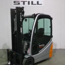 Nowy wózek widłowy STILL RX 20-16 z kabiną, srebrno-czarny z pomarańczowymi akcentami, na tle białej ściany z logo STILL i wyświetlaczem numeru.