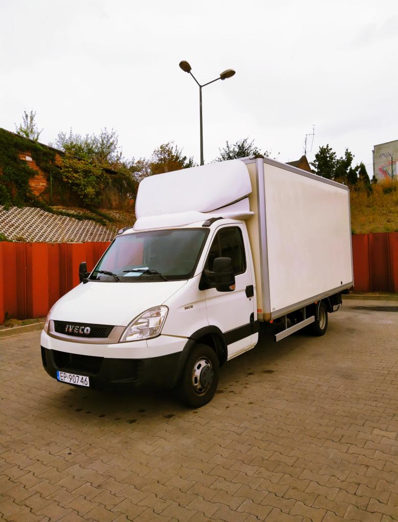 Biały samochód dostawczy Iveco z zabudową kontenerową, zaparkowany na kostce brukowej, widok z przodu pod lekkim kątem, tablica rejestracyjna EP 90746.