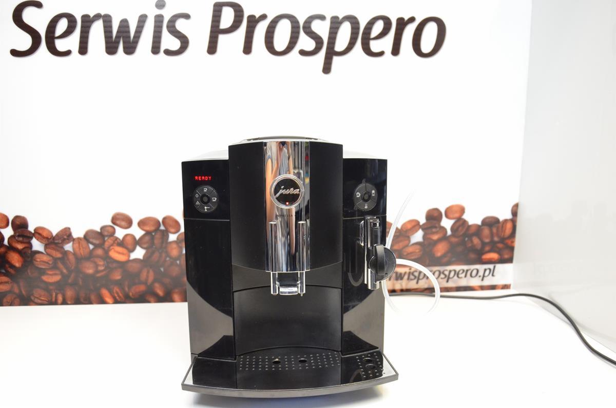 Czarny automatyczny ekspres do kawy Jura na tle reklamy Serwis Prospero z motywem ziaren kawy.