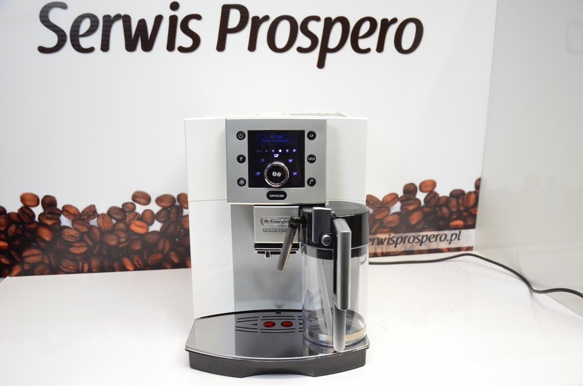 Biały automatyczny ekspres do kawy DeLonghi z pojemnikiem na mleko, na błyszczącej podstawie, z tłem przedstawiającym ziarna kawy i logo Serwis Prospero.