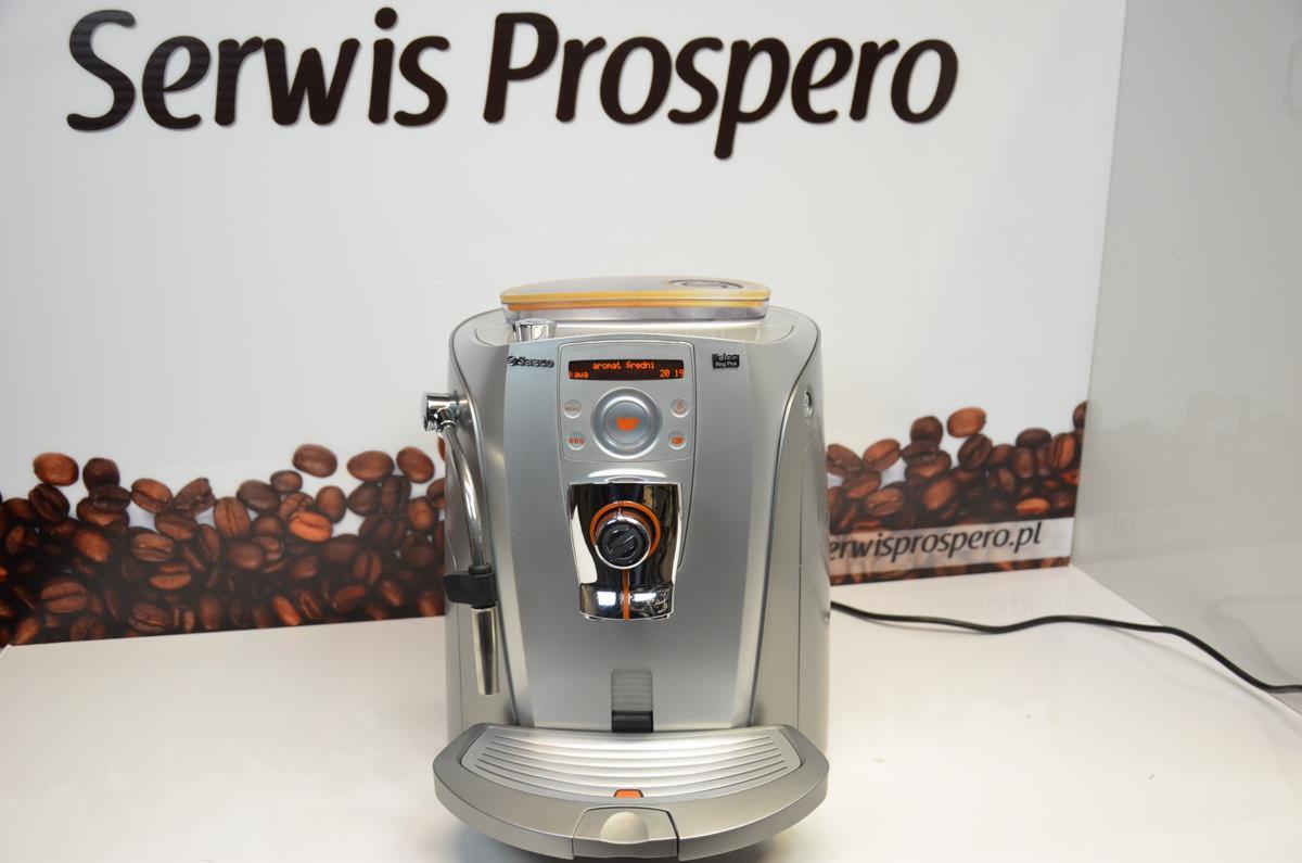 Srebrny ekspres automatyczny Saeco na białym blacie, w tle grafika z ziarnami kawy i logo Serwis Prospero.